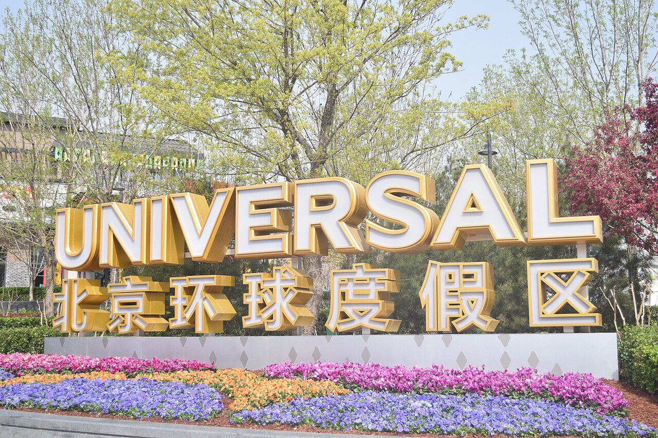 ป้ายทางเข้า UNIVERSAL 北京环球度假区 สีทองหน้า Universal Beijing Resort พร้อมแปลงดอกไม้หลากสี