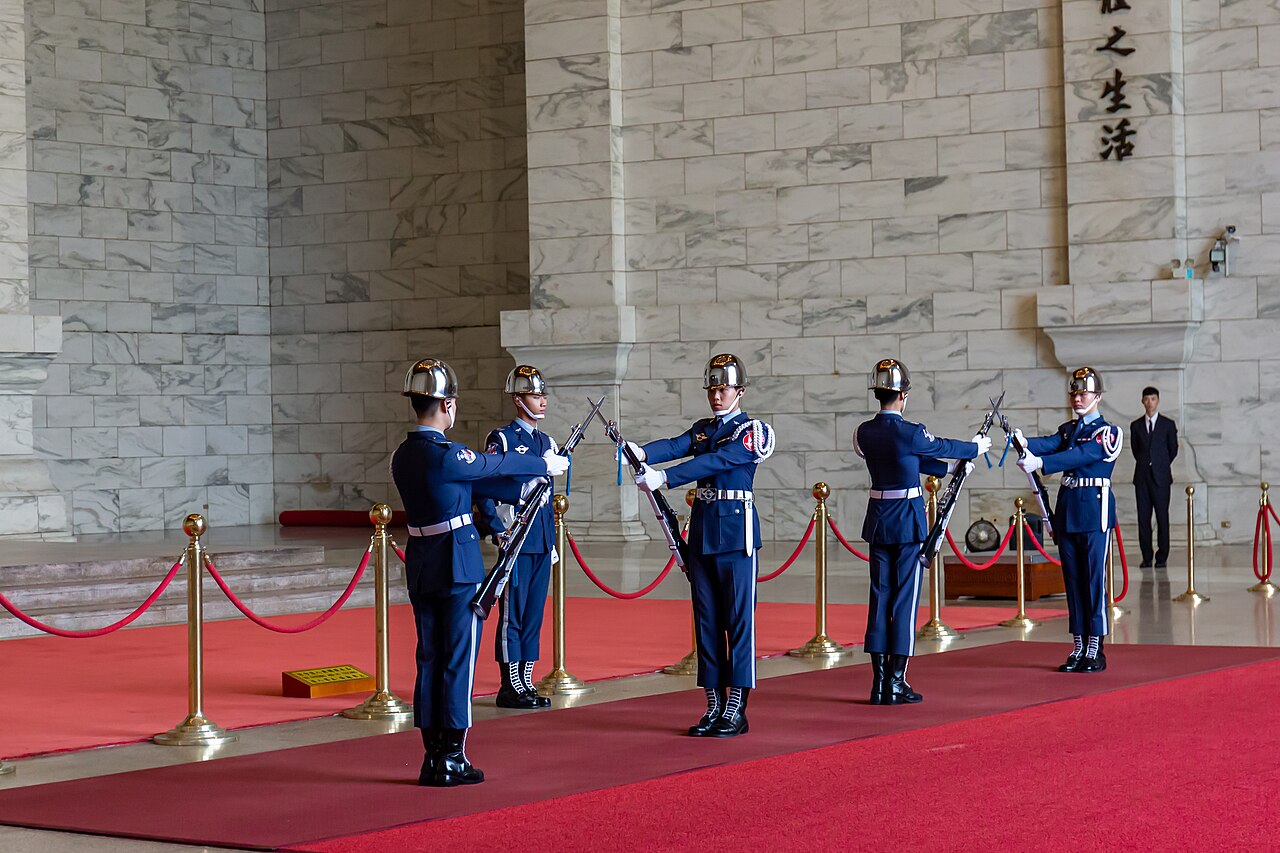 พิธีเปลี่ยนเวรทหารกองเกียรติยศในห้องโถงด้านบนอนุสรณ์สถานเจียงไคเชก ทหารห้านายในเครื่องแบบสีน้ำเงินถือปืนสวนสนามบนพรมแดง