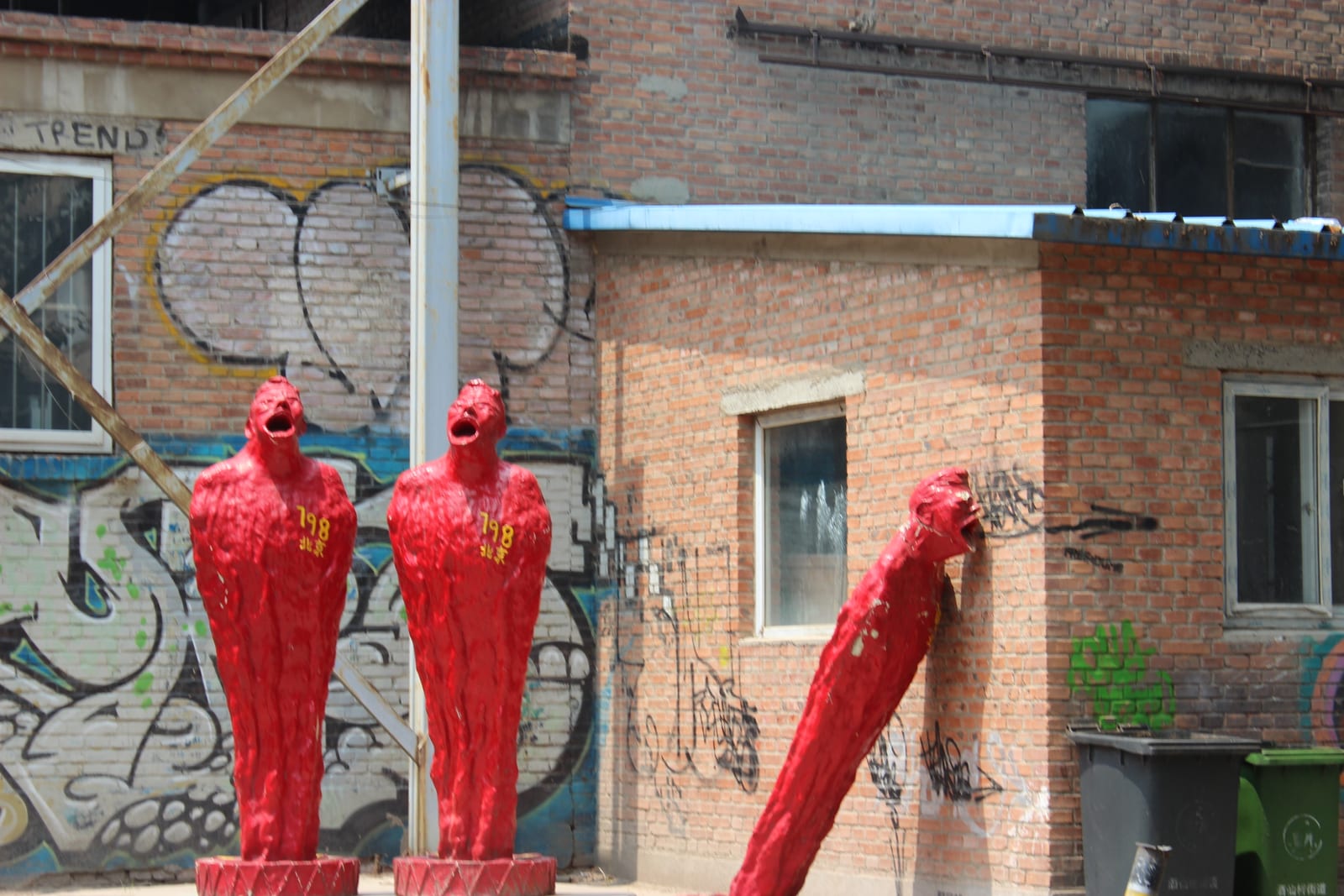 The 798 Art District in Beijing — red human sculptures standing in front of an old graffiti-covered brick factory wall, a glimpse of the art zone where cafés are scattered throughout