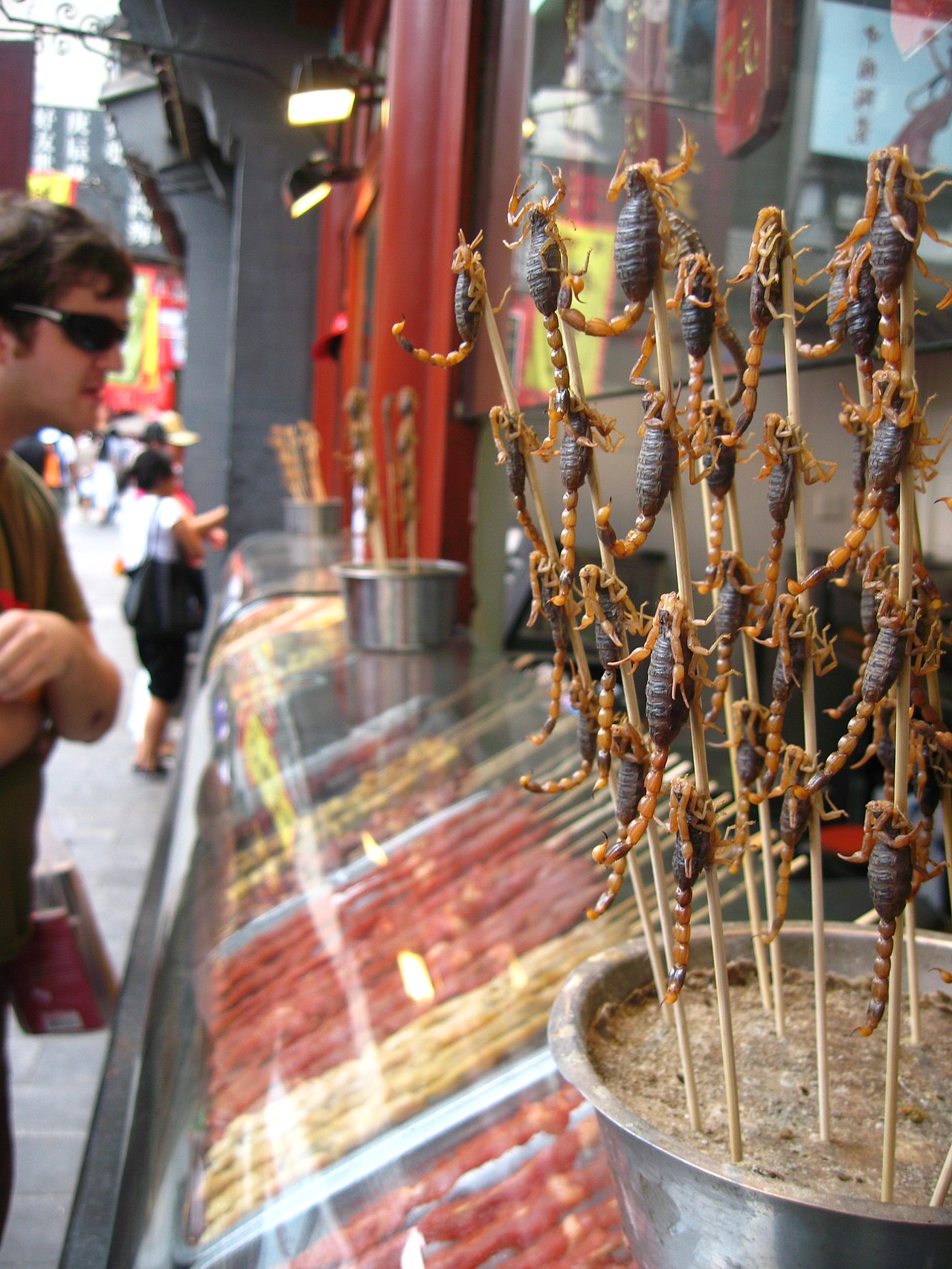 Scorpions on skewers at Wangfujing Snack Street, Beijing — a stall of novelty foods aimed at tourists, with a visitor looking on