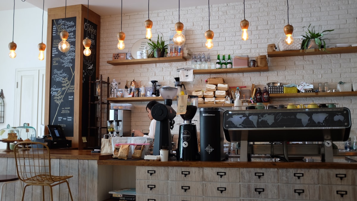 คาเฟ่บ้านเก่าในไทเป ผนังอิฐขาว ชั้นไม้ และหลอดไฟเอดิสันห้อยเหนือเคาน์เตอร์บาริสต้า