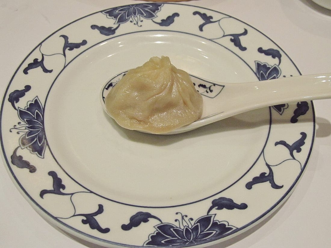 A xiaolongbao soup dumpling resting on a Chinese soup spoon, ready to be nibbled open
