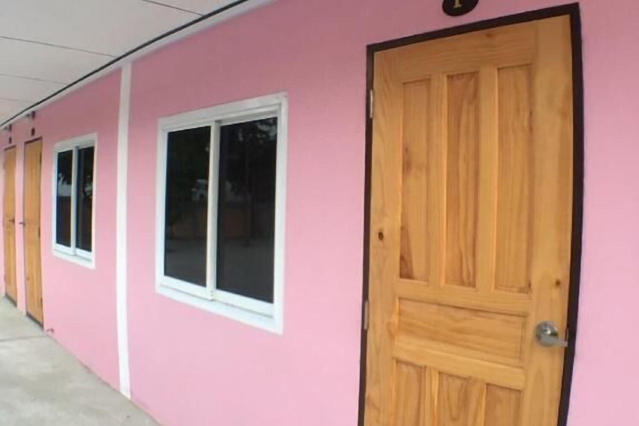 อาคารห้องพักชั้นเดียวสีชมพูของ Smile Resort อ่างทอง มีประตูไม้และที่จอดรถหน้าห้อง