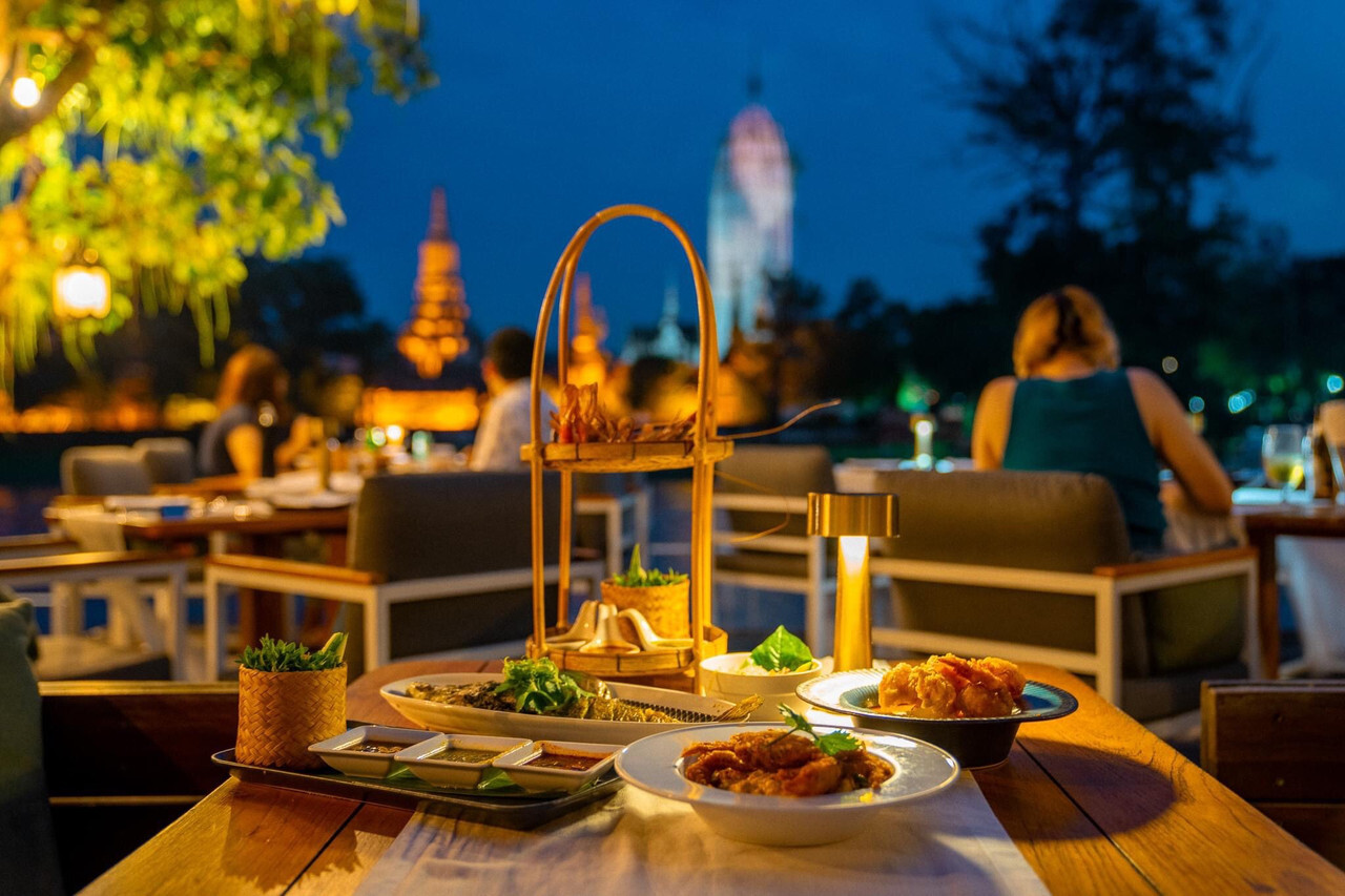 ร้านอาหารริมน้ำมองเห็นวัดพุทไธศวรรย์สว่างไฟตอนค่ำ