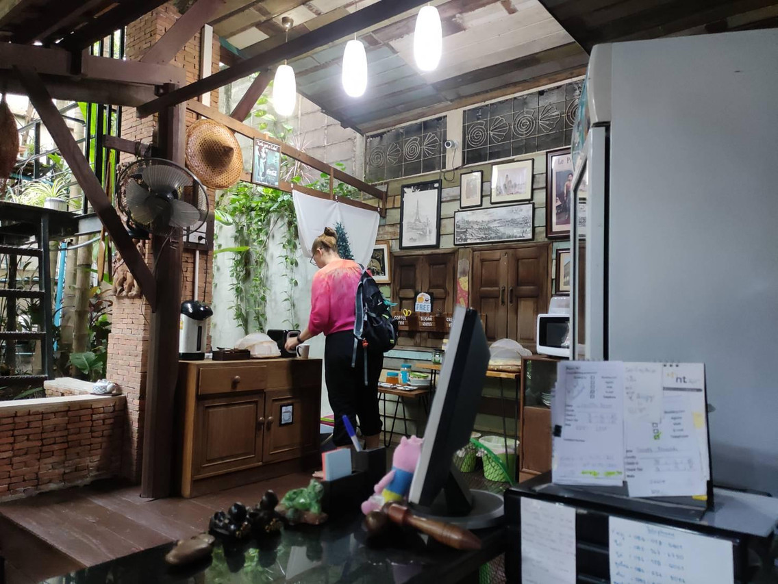 มุมอาหารเช้าในบ้านไม้เก่าของ Tamarind Guesthouse ผนังอิฐแขวนภาพอยุธยาเก่า