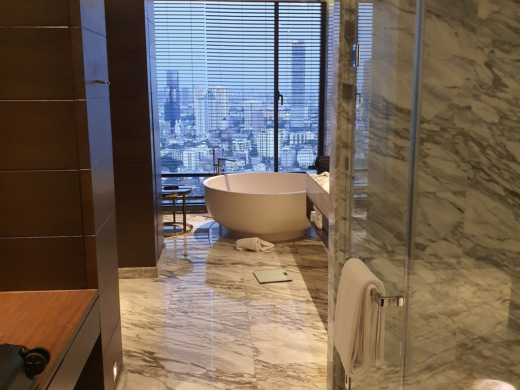 ห้องน้ำหินอ่อนพร้อมอ่างกลมและวิวเมืองกรุงเทพจากสวีท 137 Pillars Suites Bangkok