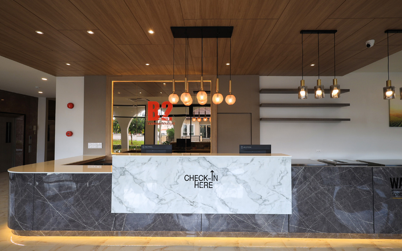 เคาน์เตอร์ต้อนรับหินอ่อน CHECK-IN HERE เพดานไม้ของ B2 Bueng Kan
