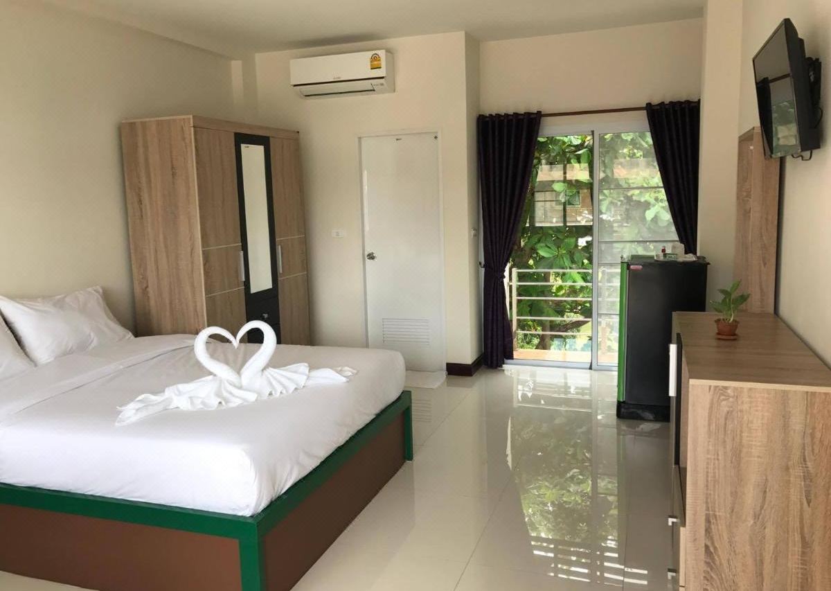 ห้องพักของ The Wisdom Residence บึงกาฬ เตียงปูผ้าขาว มีตู้เย็น ทีวี และประตูระเบียงมองเห็นสวน
