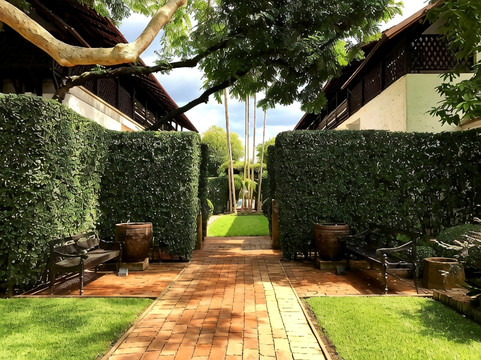 Walled garden courtyard pathway with hedged greenery and teak pavilions