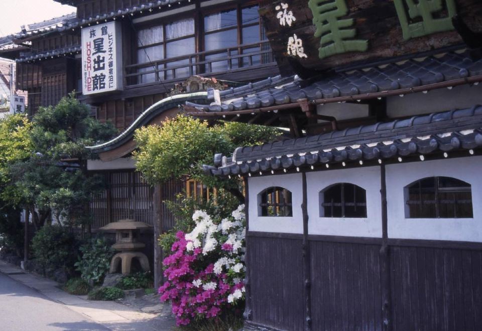 ด้านข้างอาคาร Hoshidekan พร้อมป้าย HOSHIDE 星出館 และดอกไม้หน้าประตูไม้ยุคเก่า