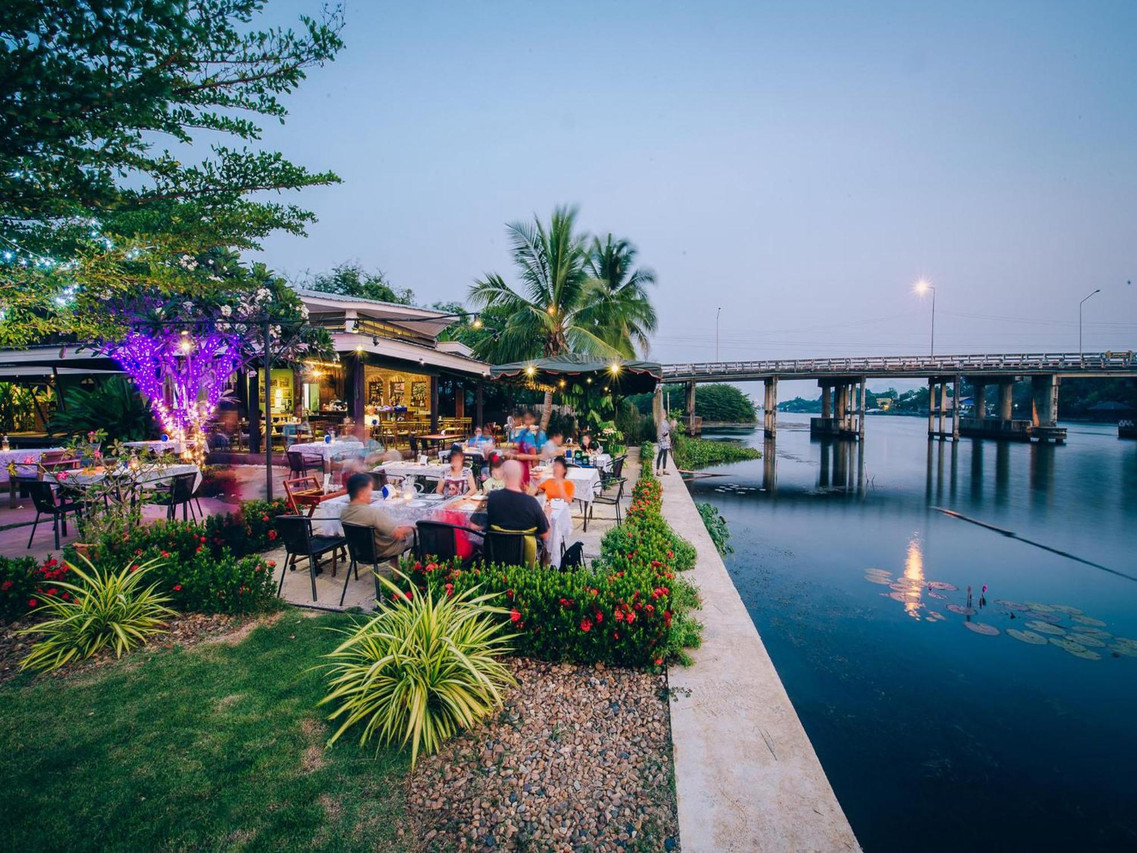 Riverbank restaurant on the River Kwai at dusk, looking across to the bridge