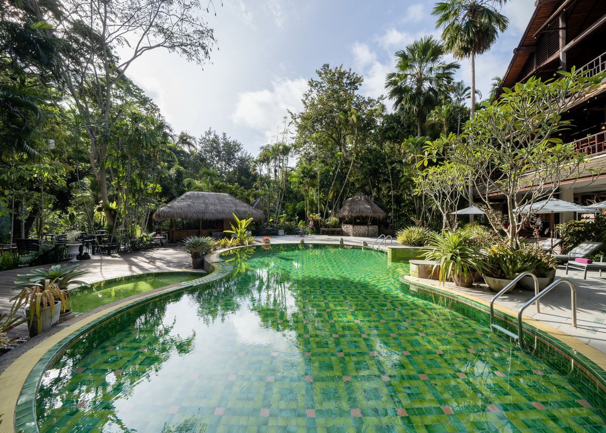 Green mosaic-tiled pool in a jungle garden with thatched salas