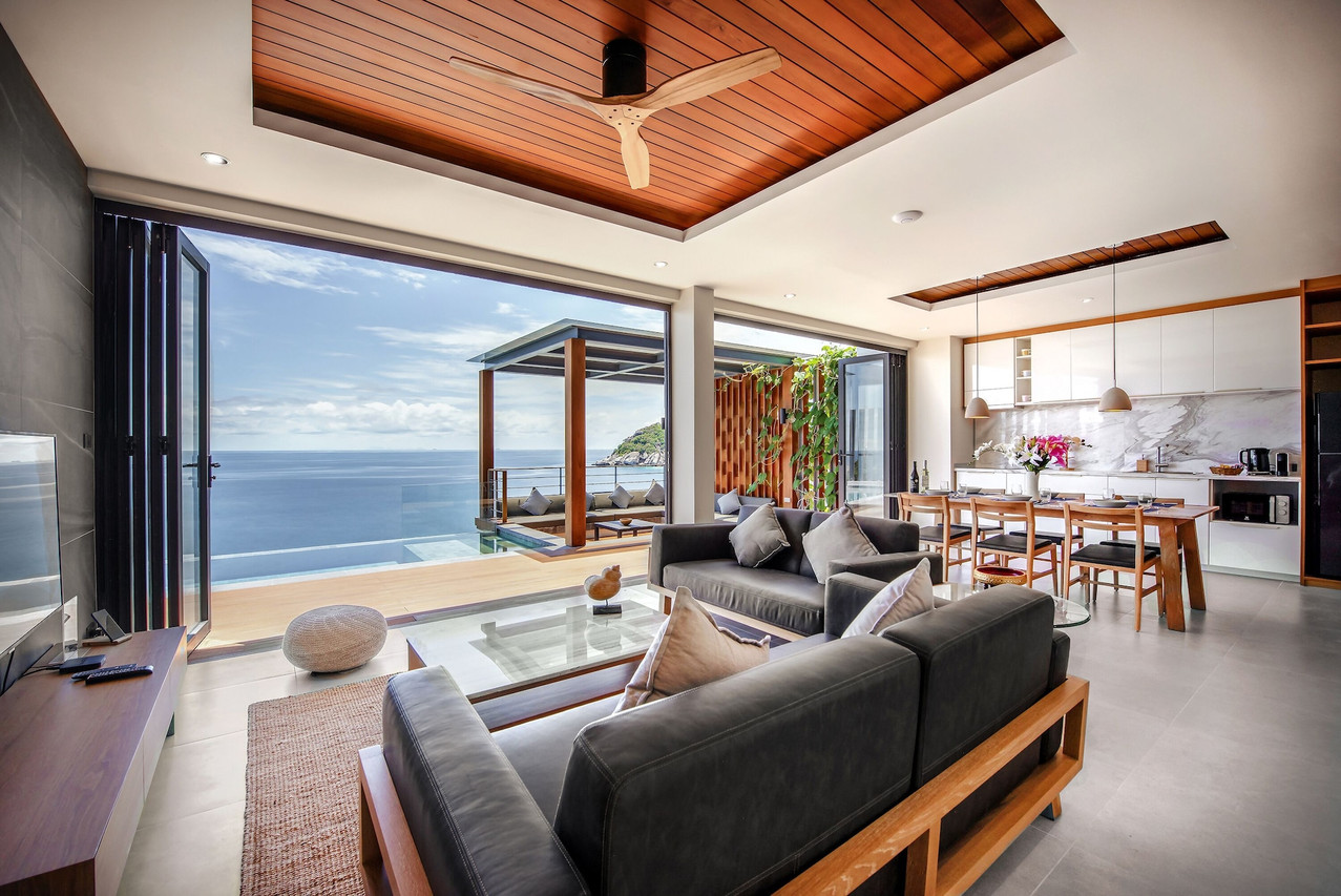 Pool villa living room opening onto an infinity pool with sea and headland views