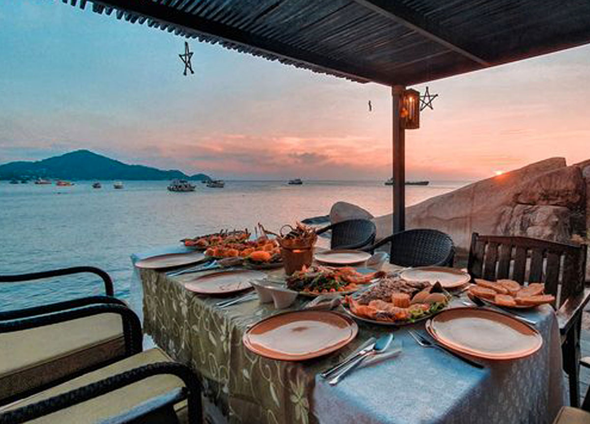 Beachfront dinner table at Rimlae Restaurant at sunset with bay and fishing boats