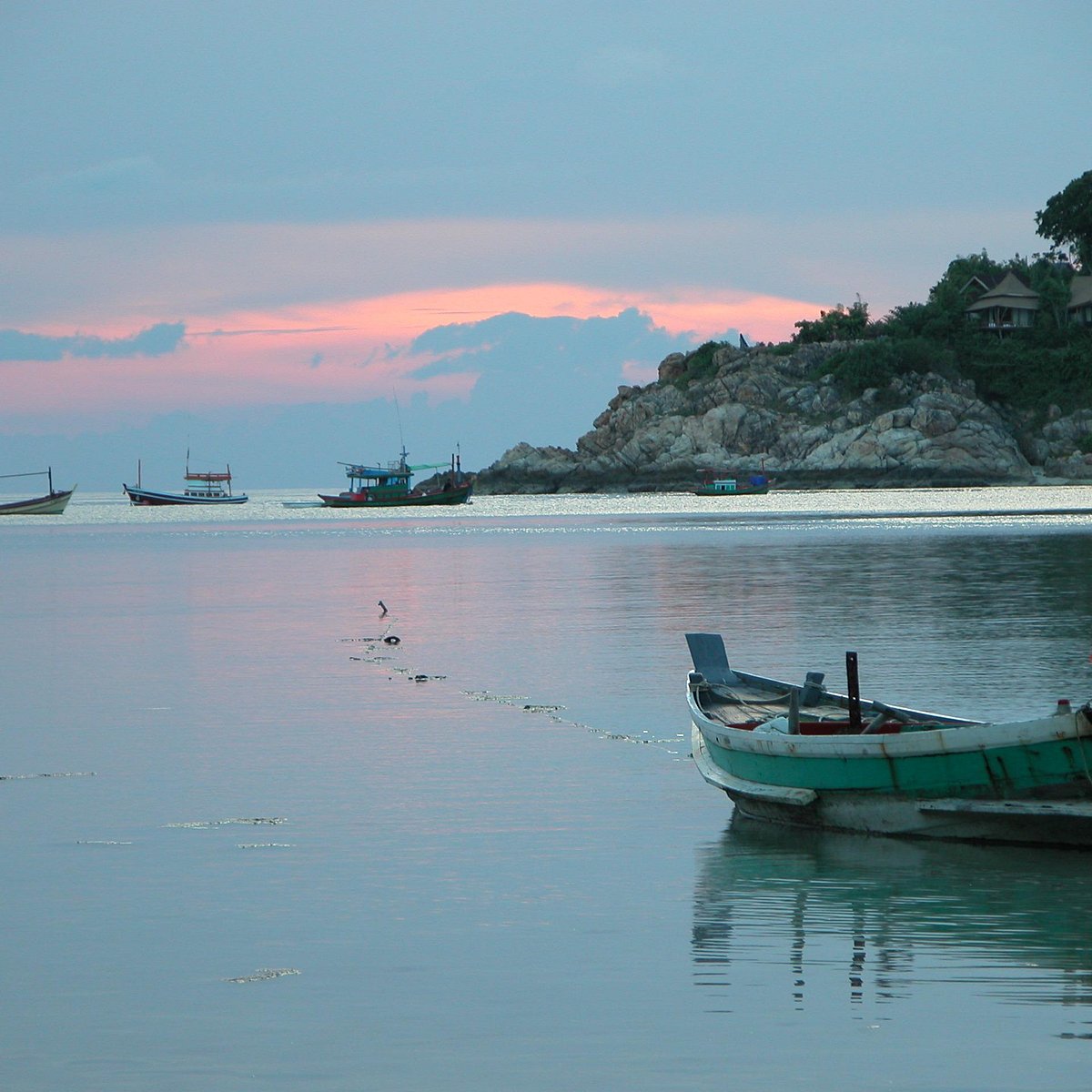 Quiet bay at nightfall, a single longtail boat and the headland with bungalows above