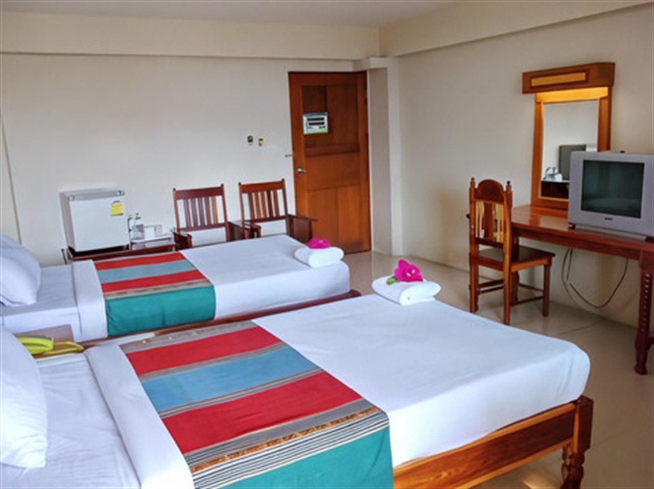 ห้องเตียงคู่ Submukda Grand Hotel ผ้าคาดเตียงลายสีสด ตู้เย็นและโต๊ะเครื่องแป้งไม้