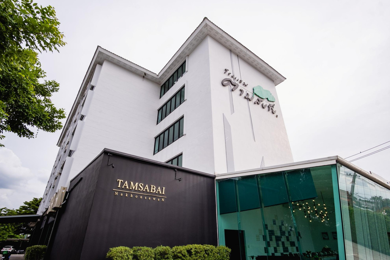 อาคารโทนขาวของ Tamsabai Hotel ถ่ายมุมเฉียง มีผนังดำติดป้าย TAMSABAI Nakhonsawan และคาเฟ่กระจกสีเขียว