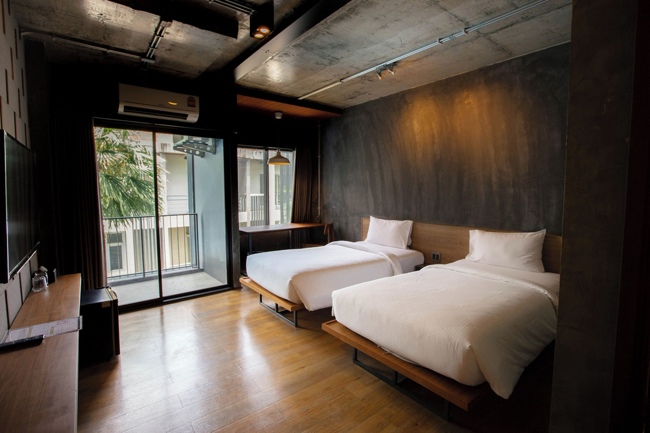 ห้อง Twin ของ Navakitel Design Hotel ผนังปูนเปลือยกับระเบียงมองเห็นต้นไม้