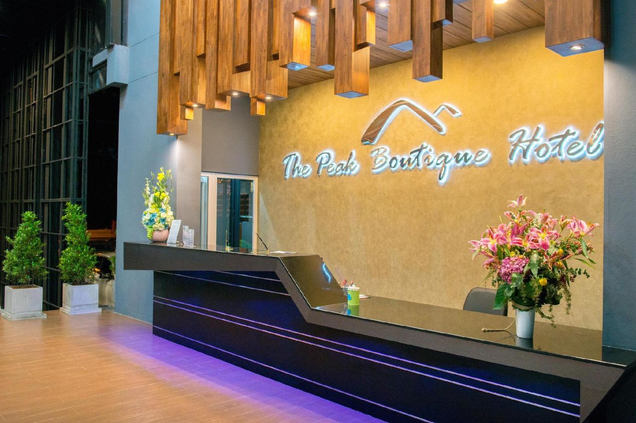 เคาน์เตอร์ต้อนรับ ฝ้าไม้ระแนง และป้ายไฟชื่อโรงแรม The Peak Boutique Hotel