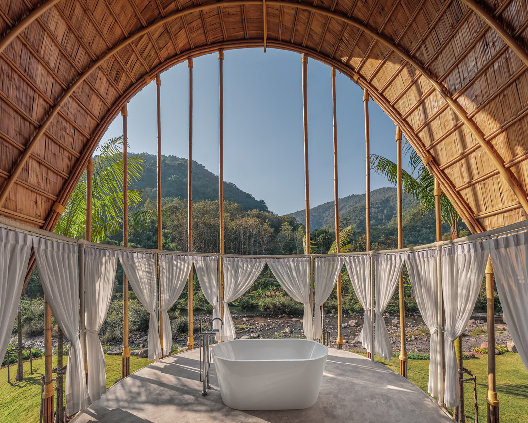 Outdoor bathtub under a curved bamboo arch looking out over the mountains and stream