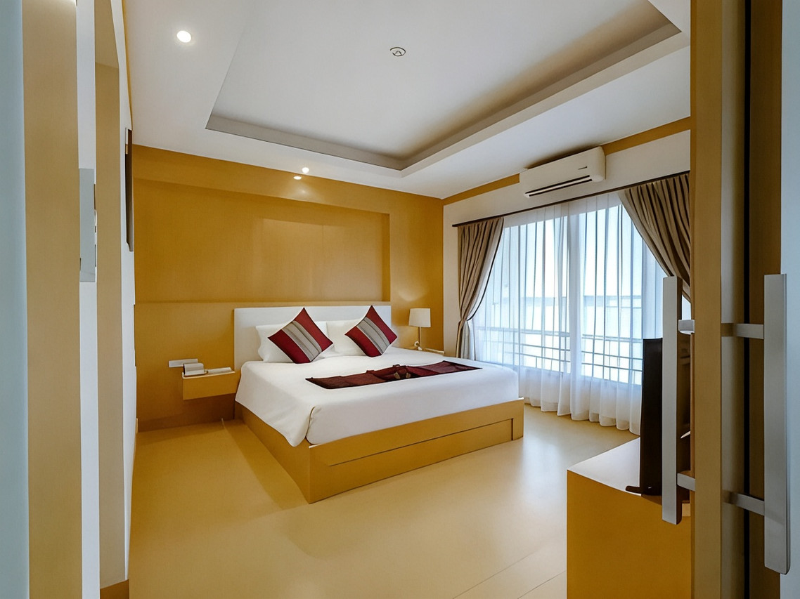 ห้องพักเตียงใหญ่ ผนังสีเหลืองอำพัน มีระเบียงและผ้าม่านโปร่ง
