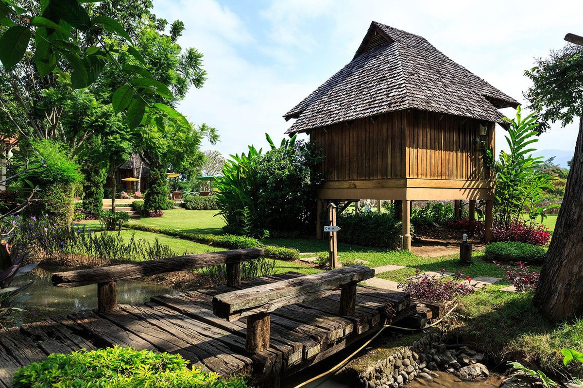 กระท่อมไม้สักยกพื้นหลังคามุงจาก กับสะพานไม้ข้ามบ่อน้ำในสวน