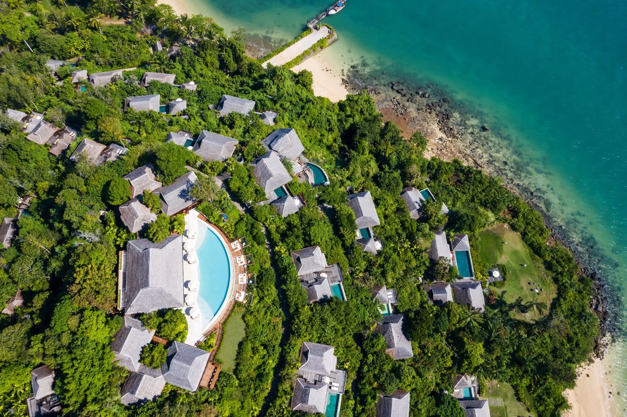 มุมสูงแสดงวิลล่าหลังคาจากของ Six Senses Yao Noi เรียงตามเนินเขาริมหาด