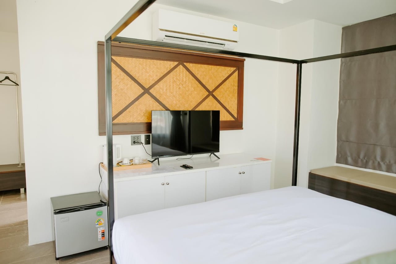 ห้องพักดีไซน์ขาว-ไม้ เตียงโครงเหล็กสี่เสา ตู้เย็นเล็ก ทีวีจอแบน