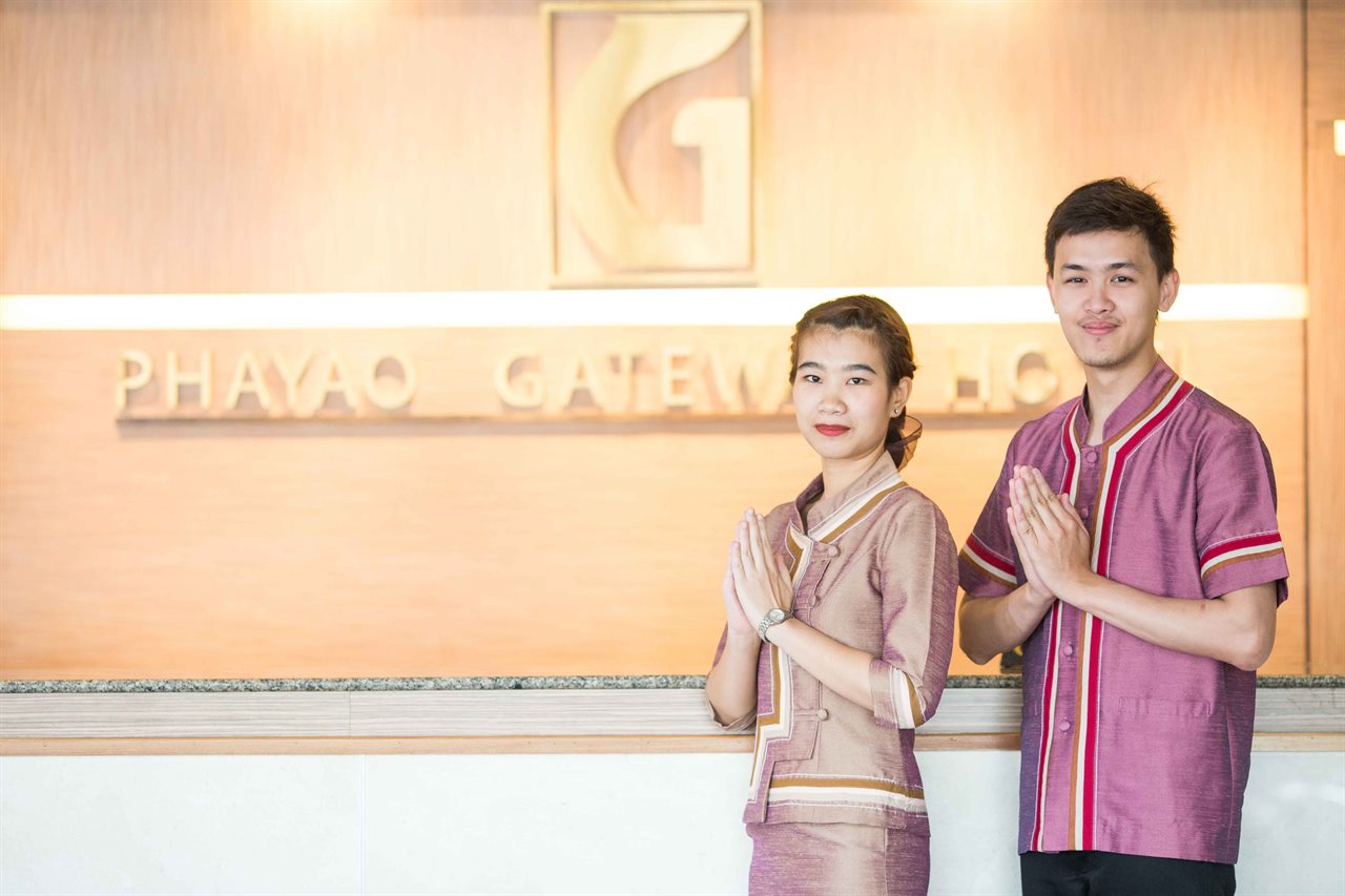 พนักงานสองคนในชุดไทยไหว้รับหน้าเคาน์เตอร์ที่มีป้าย Phayao Gateway Hotel