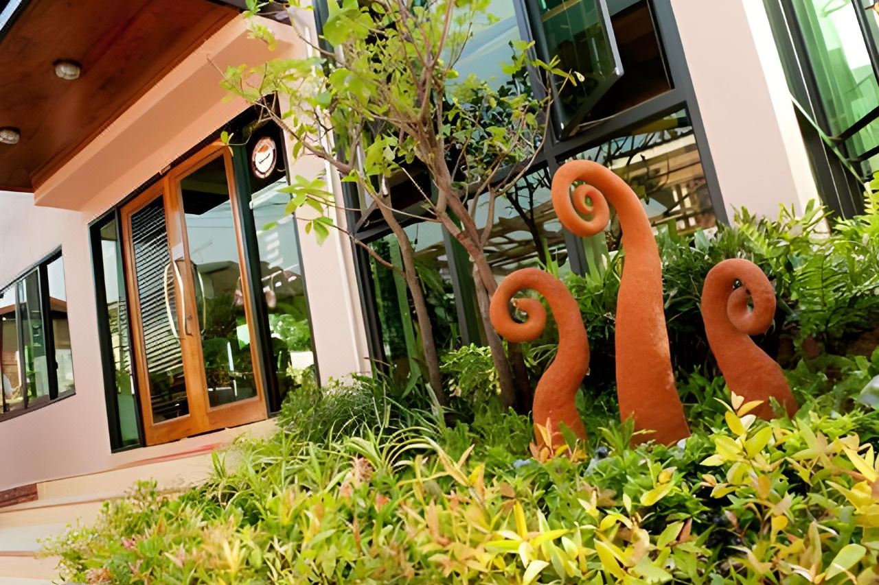 ทางเข้าวิลล่าประตูไม้กับงานปั้นรูปยอดเฟิร์นสีส้มในสวน Kwan Phayao Villa