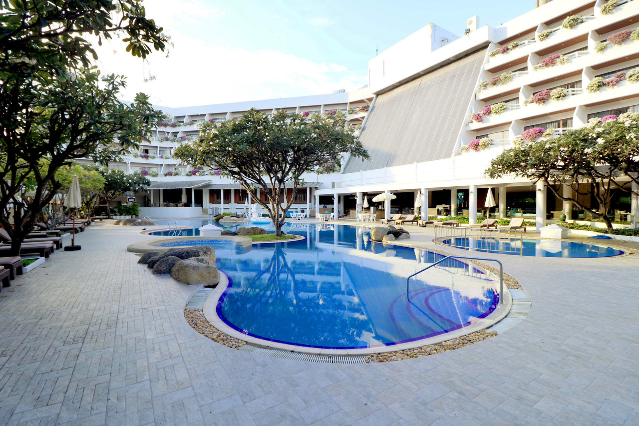 Curved outdoor swimming pool beside the flower-draped Methavalai building