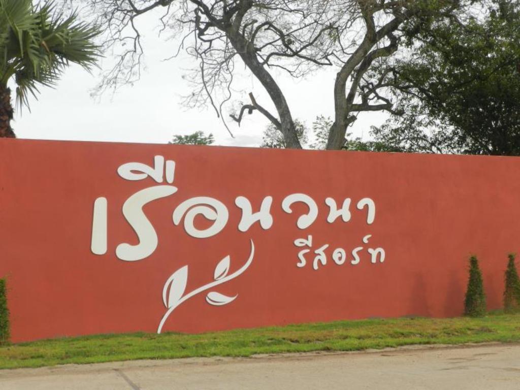 ป้ายทางเข้าเรือนวนา รีสอร์ท พิจิตร พื้นสีส้มอิฐกับต้นไม้ใหญ่