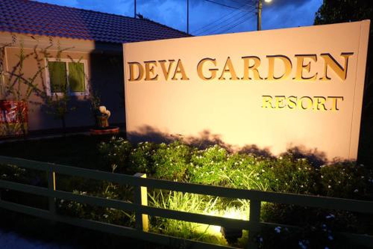 ป้าย Deva Garden Resort ส่องไฟตอนค่ำพร้อมสวนดอกไม้ด้านหน้า