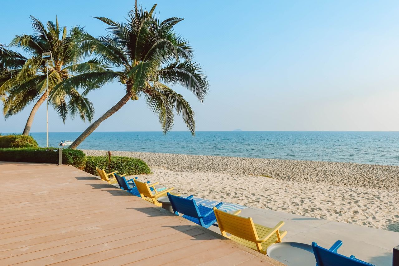 ลานไม้ริมหาดพร้อมเก้าอี้สีฟ้า-เหลือง มองเห็นทะเลและเกาะไกลๆ ที่ Novotel Rayong Rim Pae