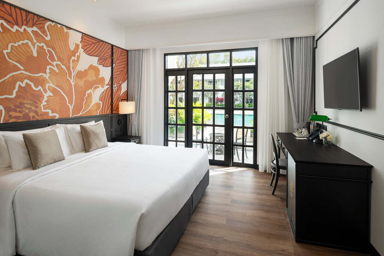 ห้องพัก Deluxe ของ Indochina Hotel มีประตูบานเฟี้ยมเปิดออกสระว่ายน้ำ หัวเตียงลายดอกไม้สีส้ม