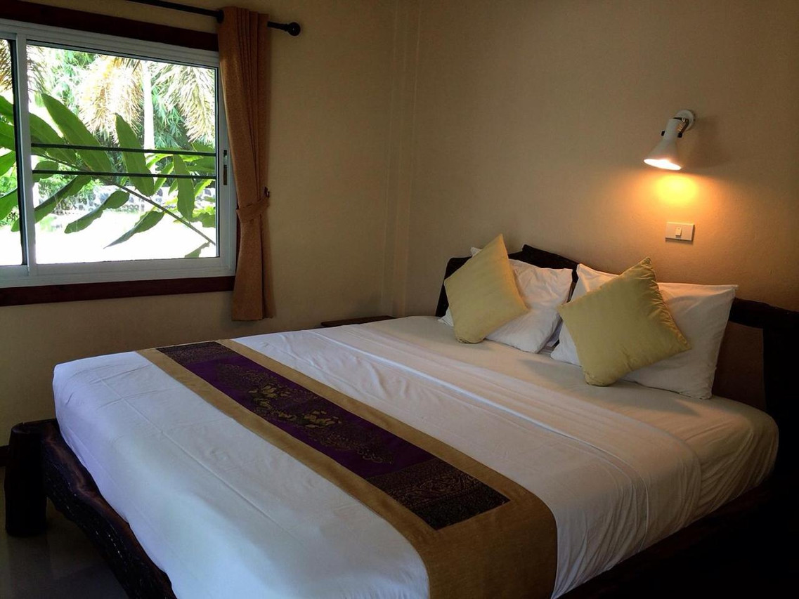 Bungalow guest room with a large bed, Thai silk runner and a garden-view window
