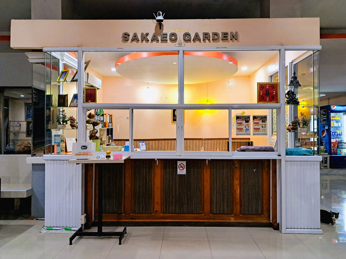 เคาน์เตอร์ต้อนรับของ Sakaeo Garden Hotel มีป้าย SAKAEO GARDEN อยู่เหนือเคาน์เตอร์ไม้