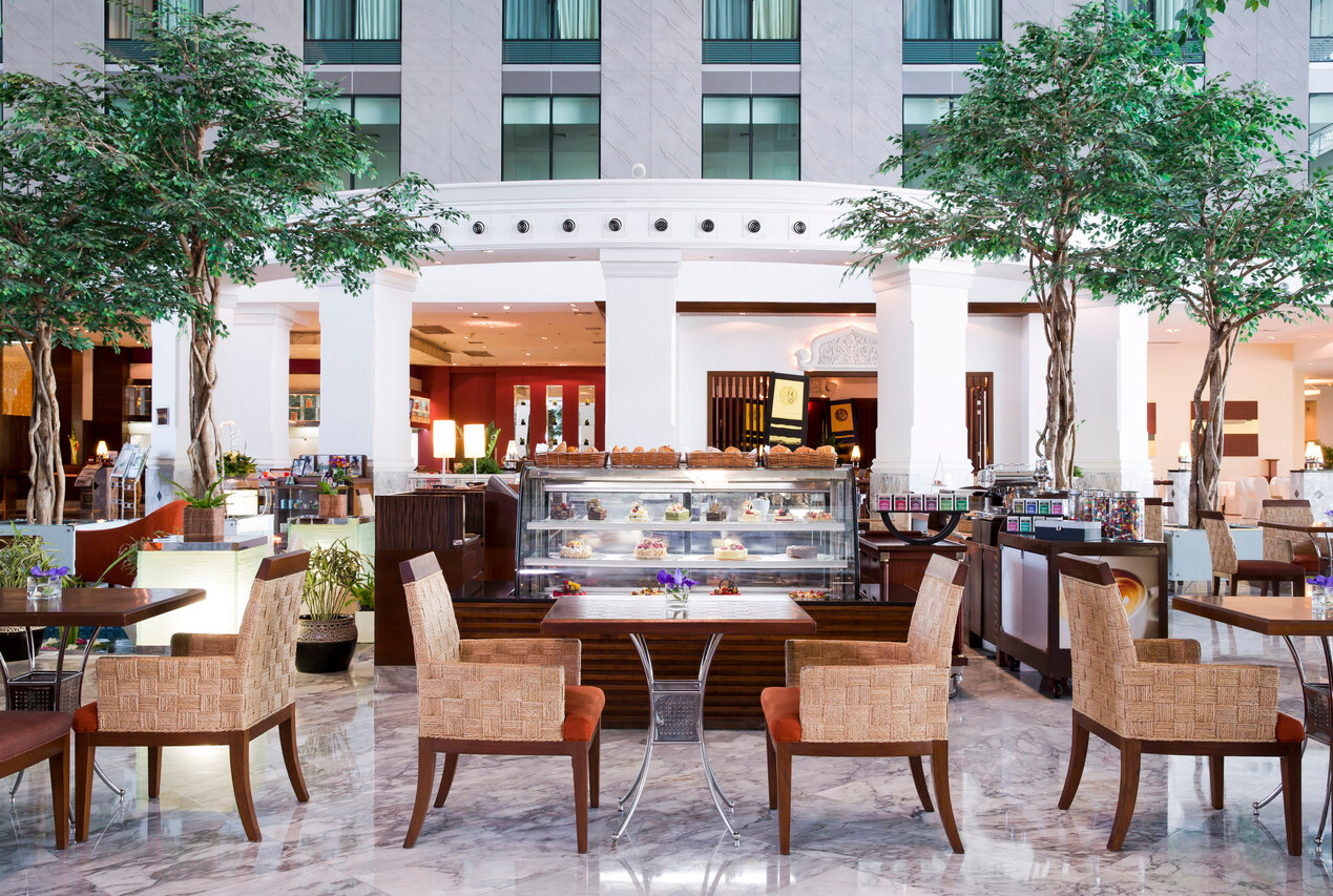 โถง atrium กลางโรงแรม พื้นหินอ่อน เสาขาว ต้นไม้สูงกลางล็อบบี้