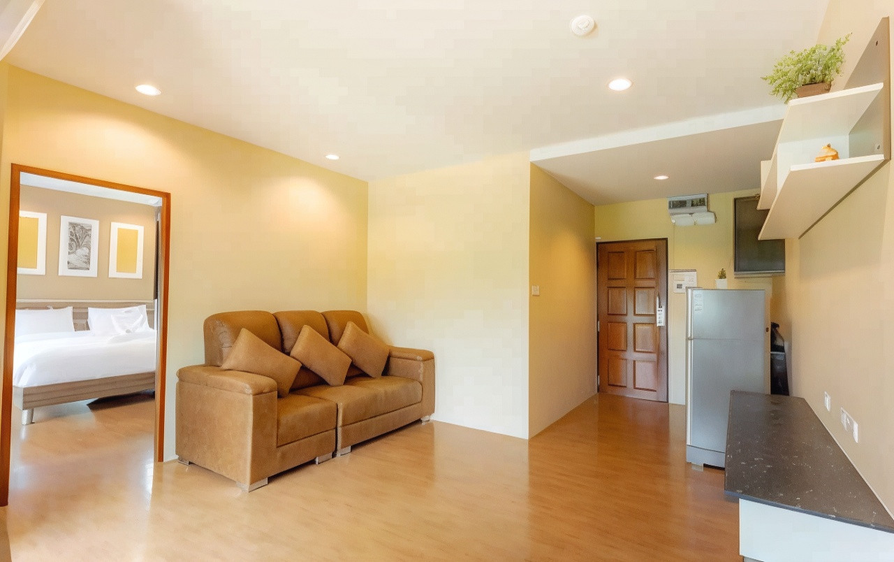 Suite living room with leather sofa, kitchenette and fridge, bedroom with large bed beyond