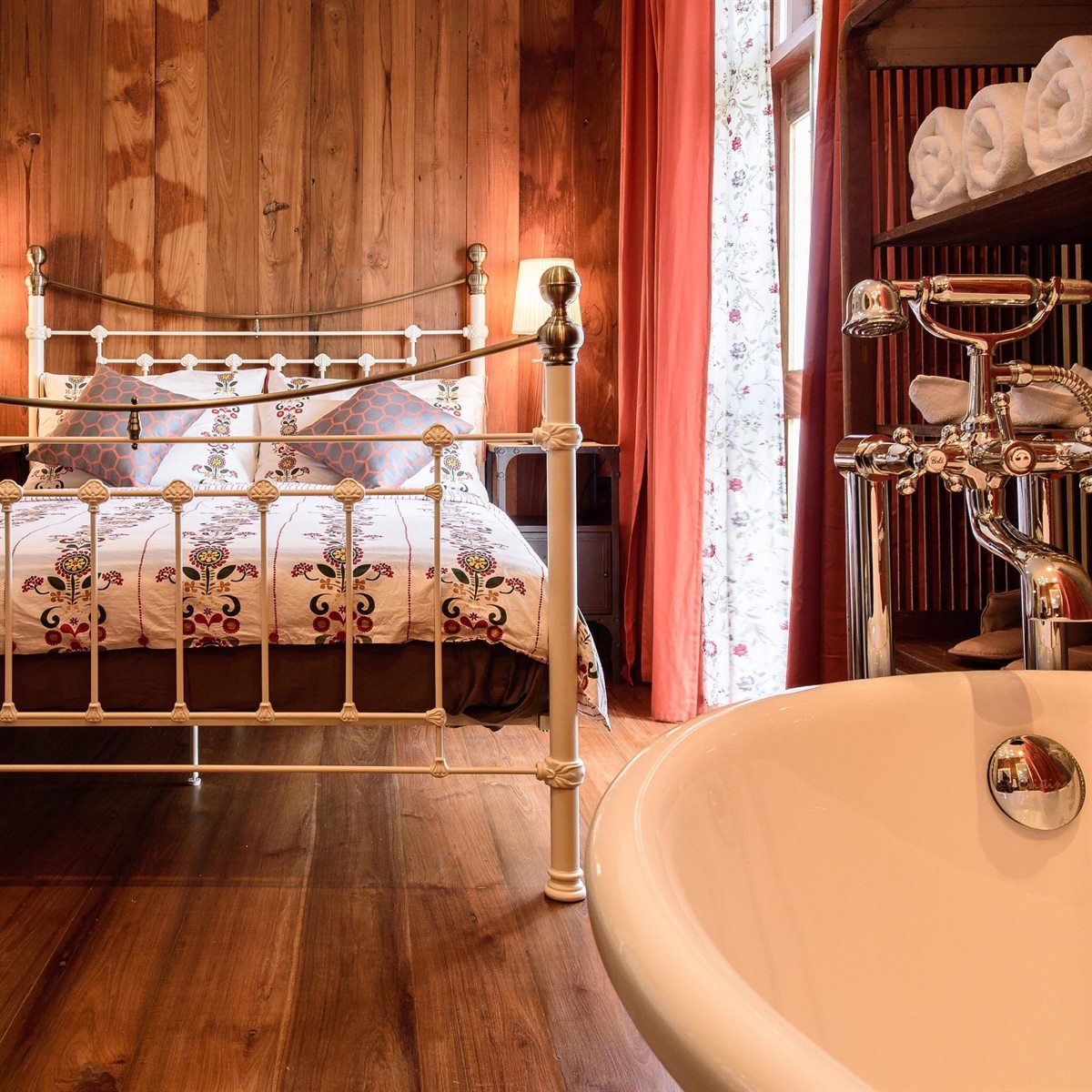 Suite with a white wrought-iron bed and a clawfoot bathtub against timber walls