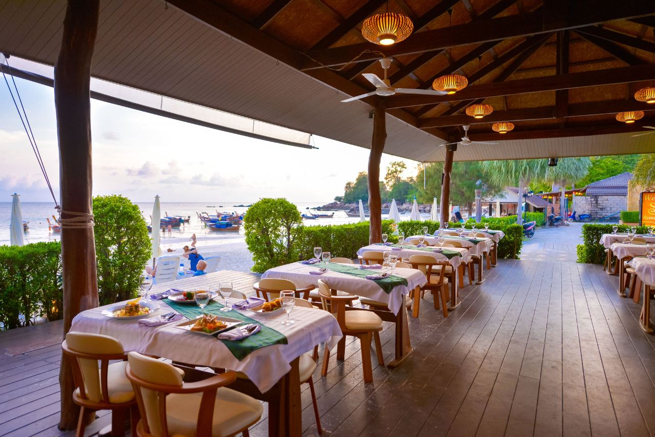 ร้านอาหารริมทะเลแบบเปิดโล่งมองเห็นหาดและเรือหางยาวช่วงพระอาทิตย์ตก