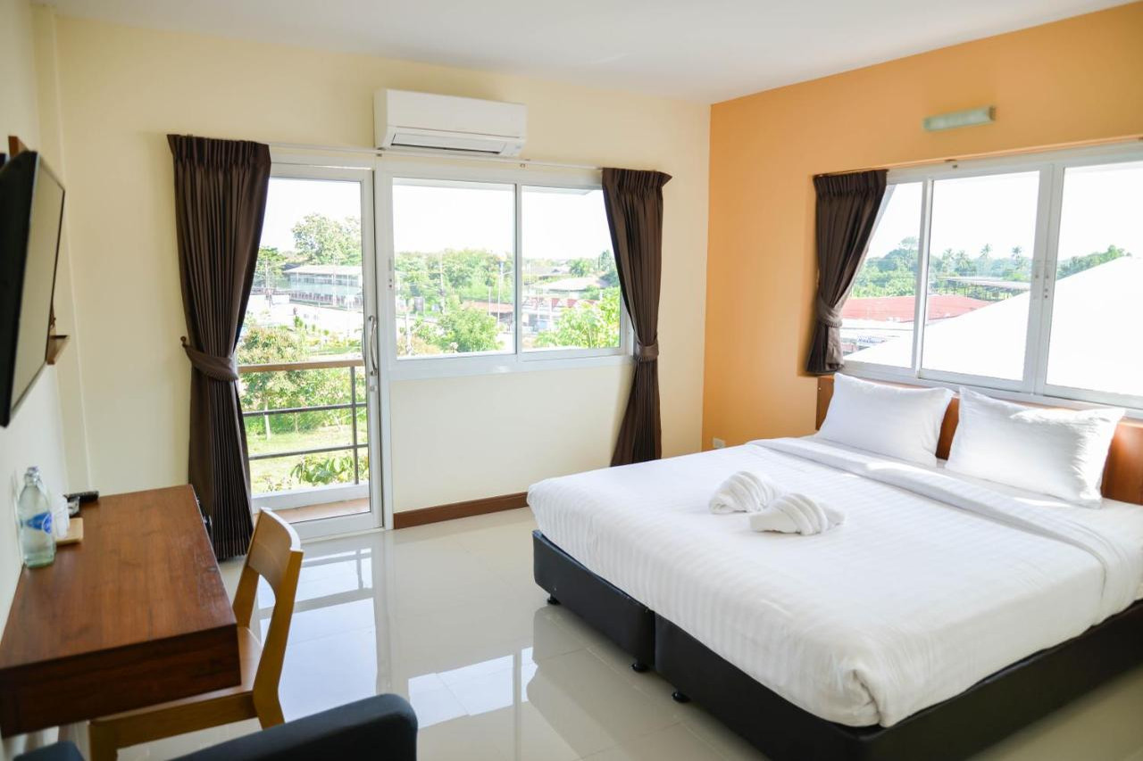 ห้อง Standard ของ Thaimit Resort เตียงใหญ่ ผนังคาดส้ม พื้นกระเบื้องขาว ประตูกระจกบานเลื่อนออกระเบียงมองวิวเมือง โต๊ะทำงานไม้